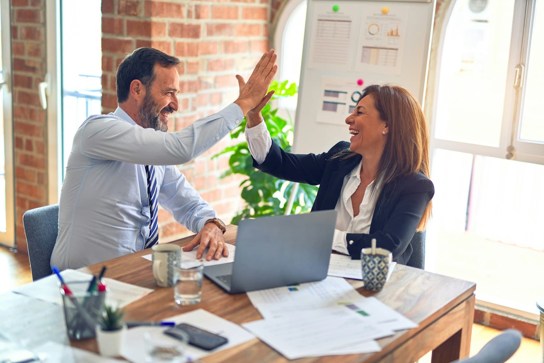 Two professionals high-fiving across a meeting table, celebrating finished work
