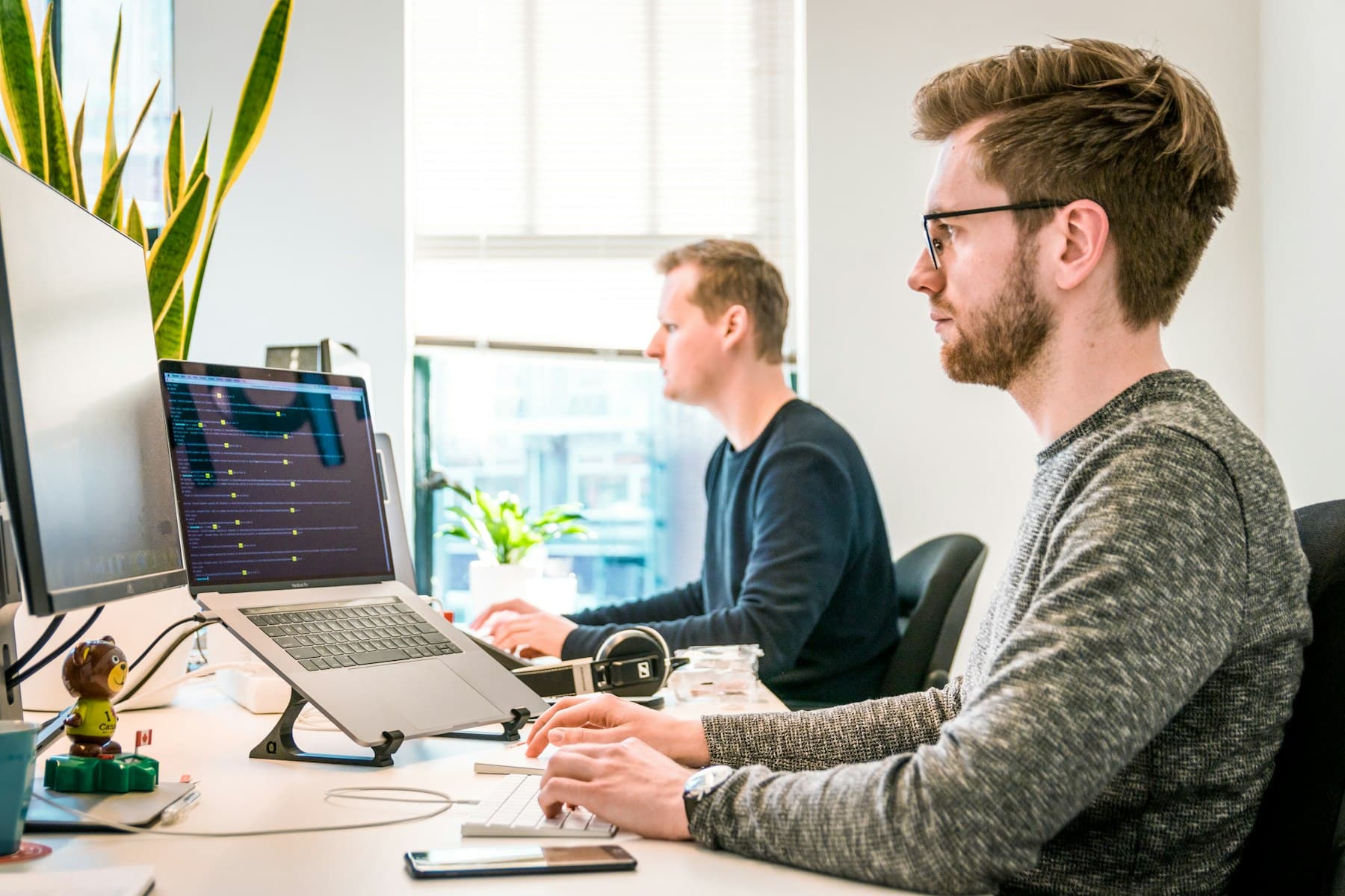 Two software engineers working at monitors in a light office, the build work of an agentic AI lab for colleges