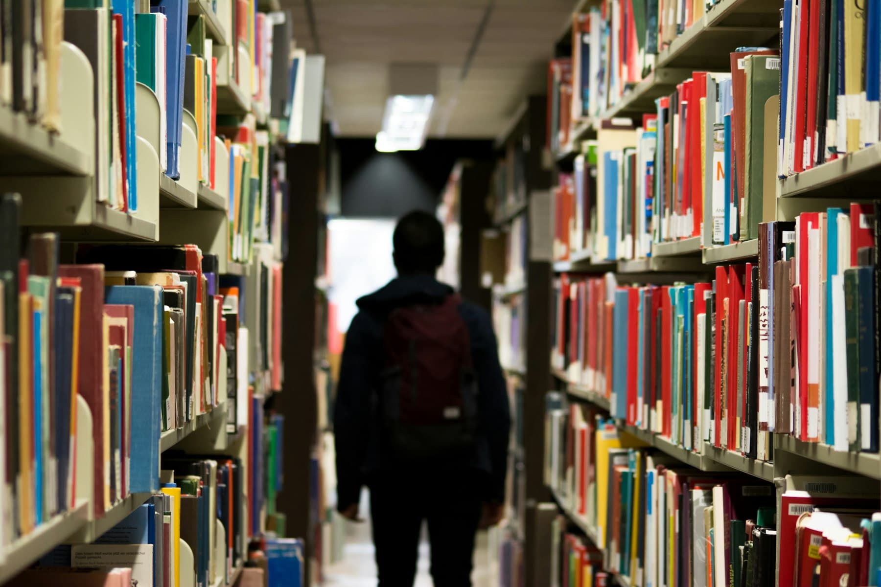 A reader walking down a library aisle between full bookshelves